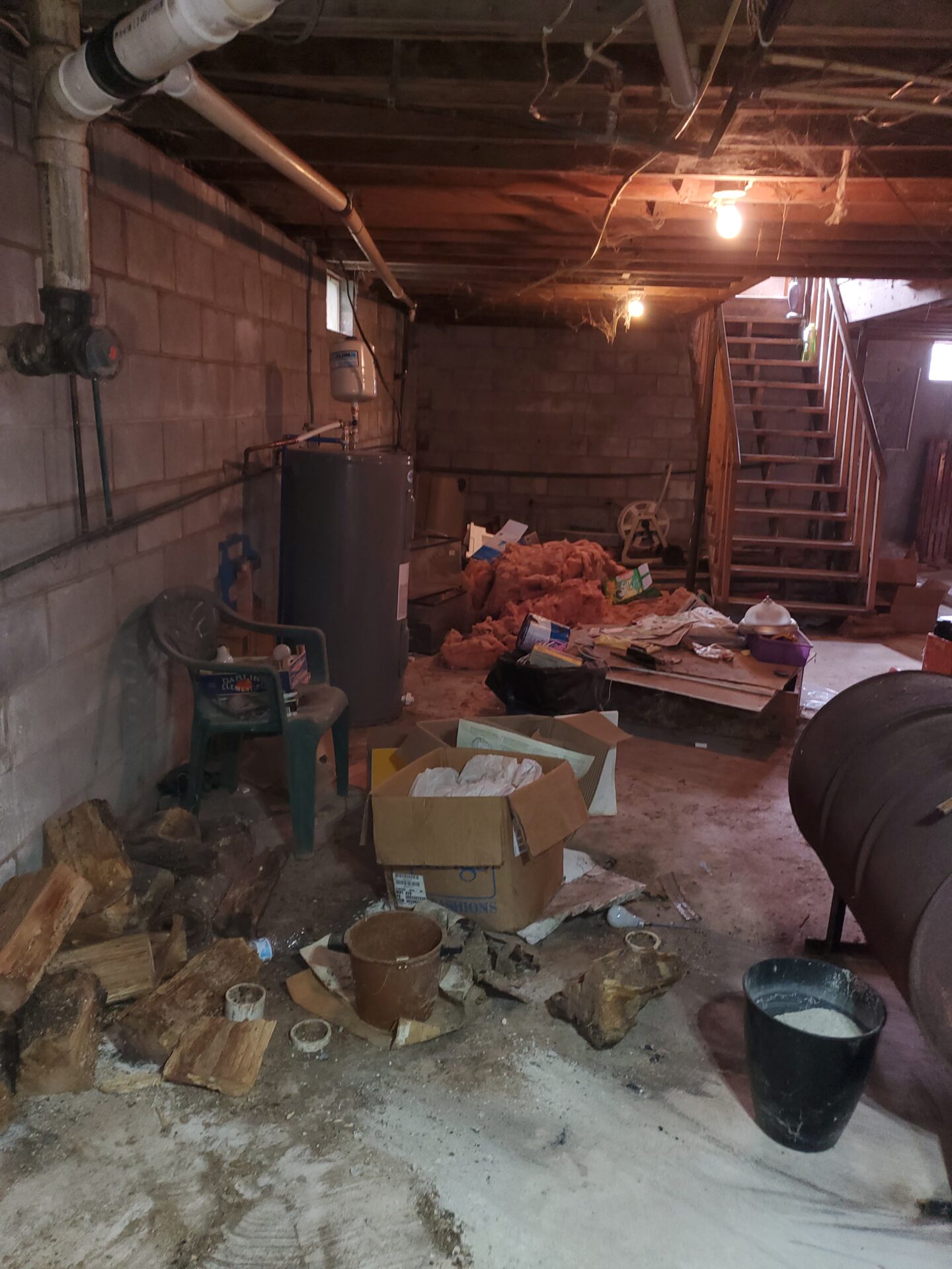 Cluttered basement with exposed pipes, wood logs, and scattered debris. Image is rotated